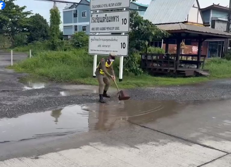 ด.ต.รักเกียรติ ใช้ไม้ตักขยะตักน้ำที่ท่วมขังออกจากผิวทาง เพื่อป้องกันการเกิดอุบัติเหตุแก่รถที่ใช้เส้นทาง